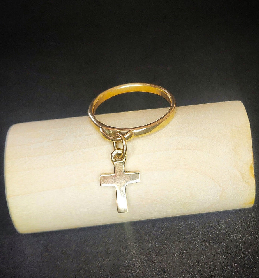 Solid gold dangly charm ring with crucifix on a wooden block