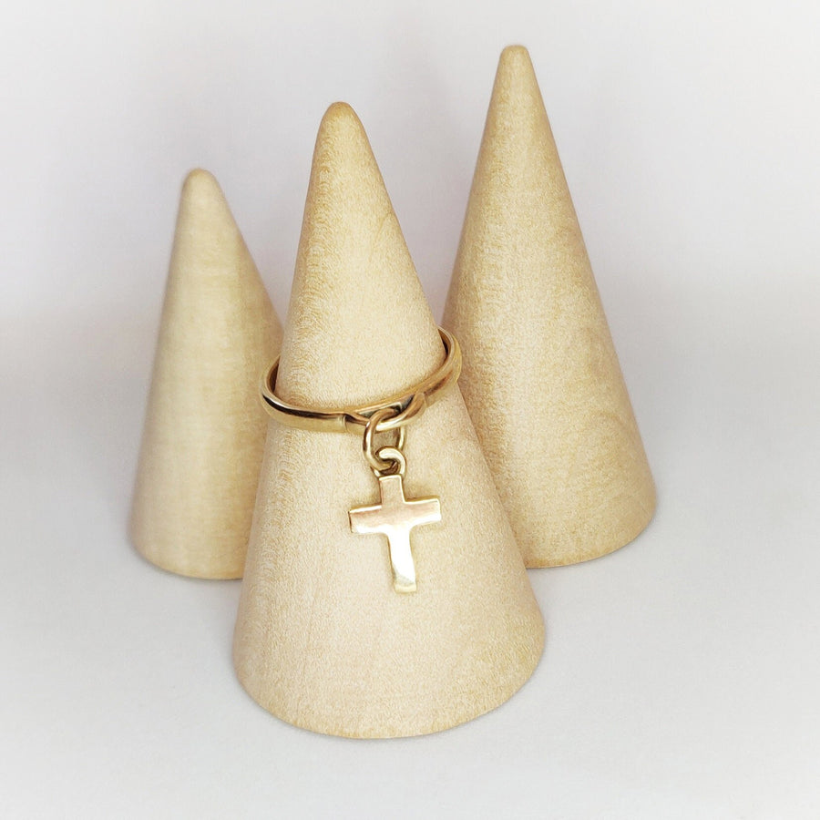 Gold ring with cross charm on a wooden display against a white background.