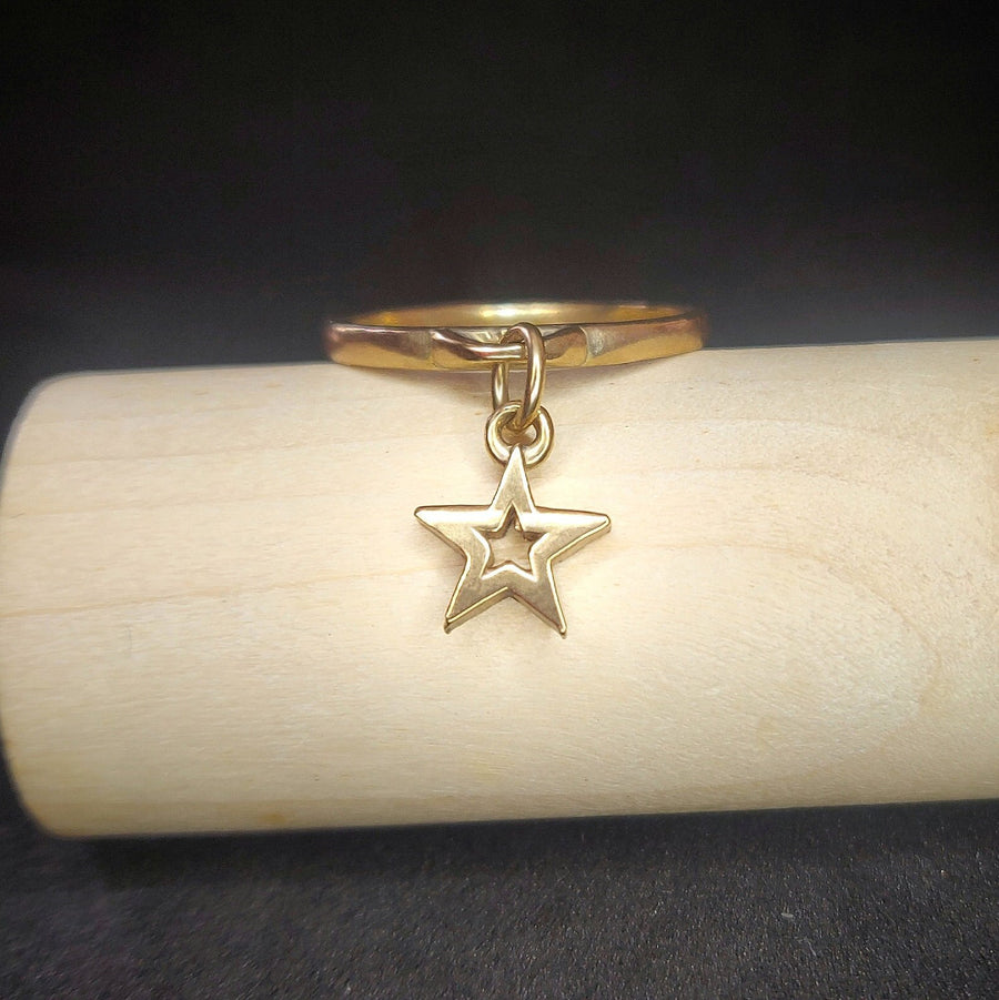 Solid gold charm ring with a gold star on a wooden display.