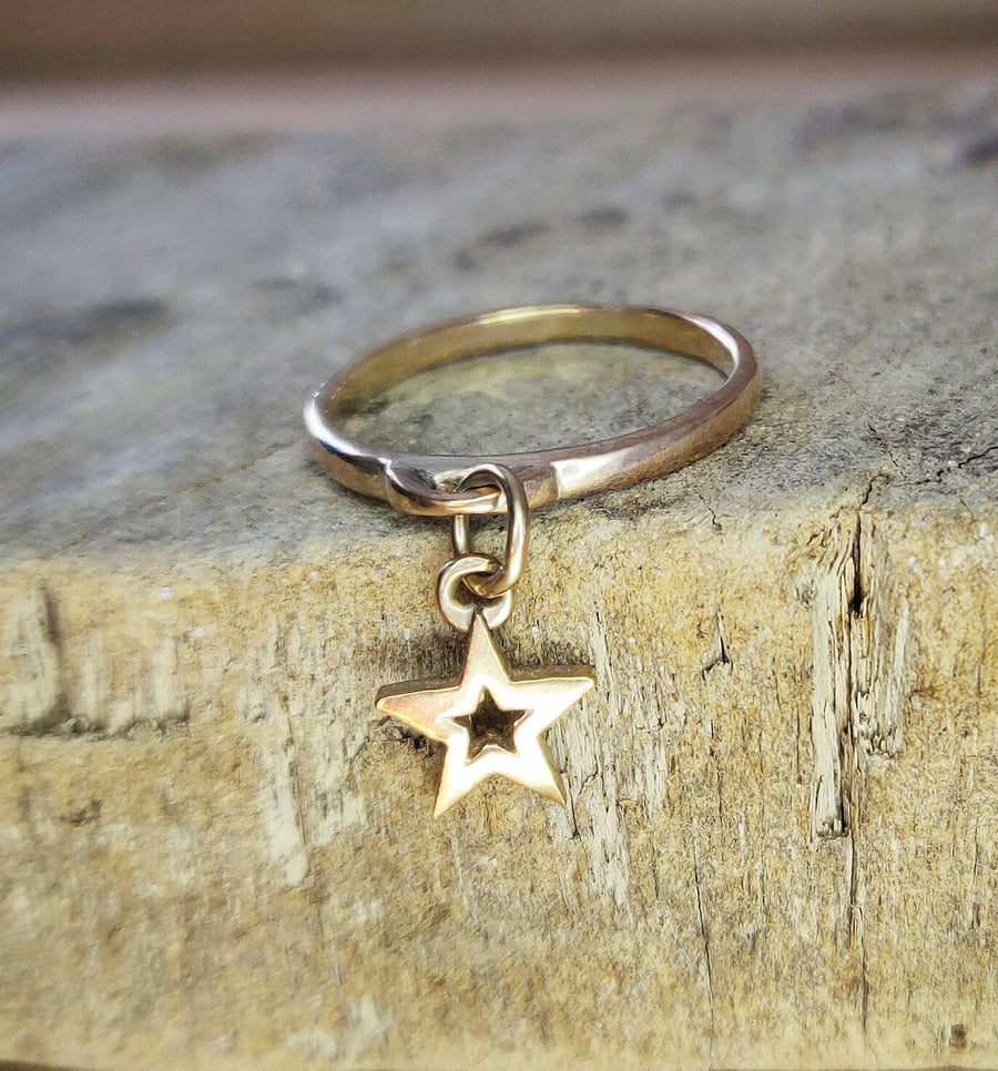 Solid gold dangle ring with a gold star charm on a wooden block.