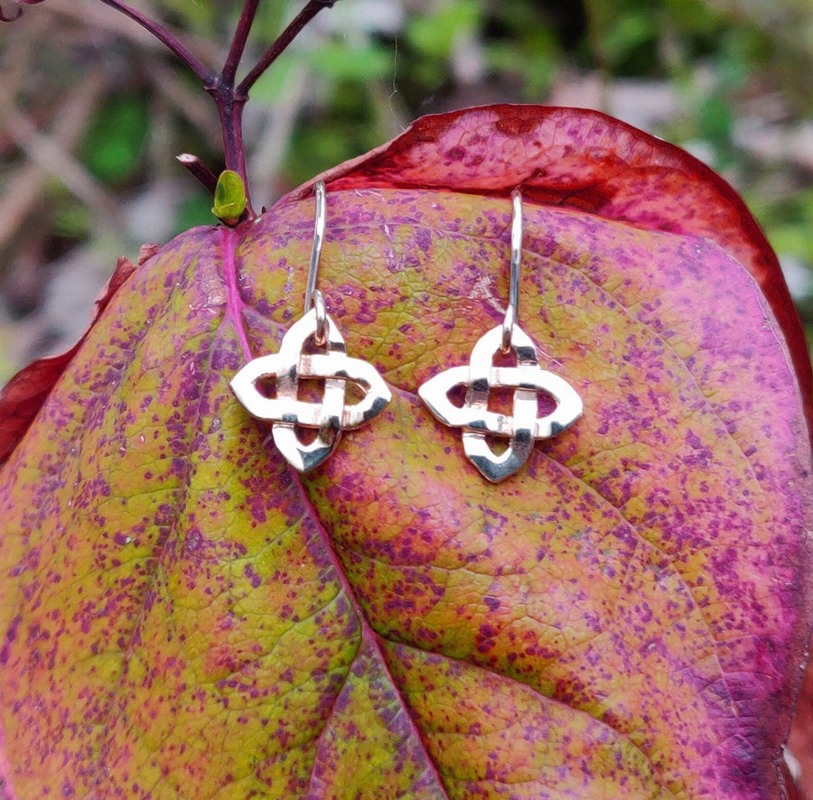 Pair of celtic knot dangle solid gold earrings on a leaf.