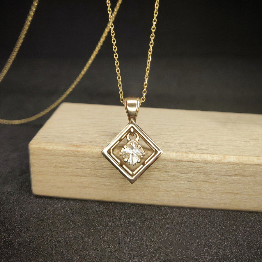 Square gold necklace with a white sapphire hanging against a wooden background.