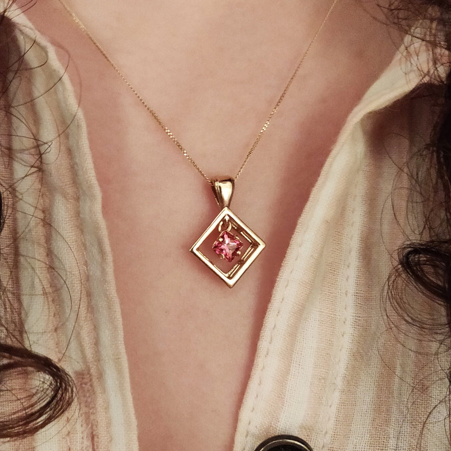 Gold diamond shaped pendant and chain with pink sapphire being worn.