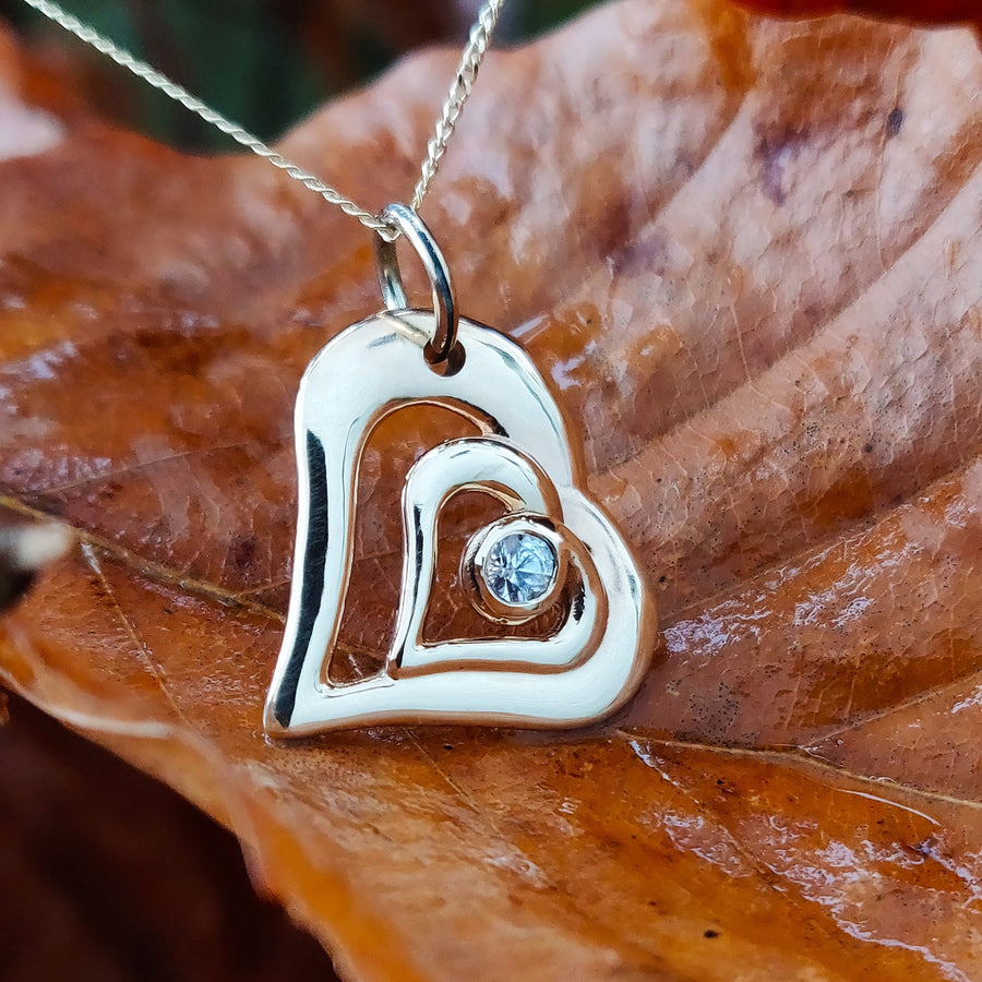 Gold and diamond sweetheart pendant with gold chain on a leaf.
