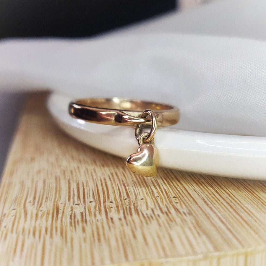 Close up of a solid gold heart charm ring on a dish