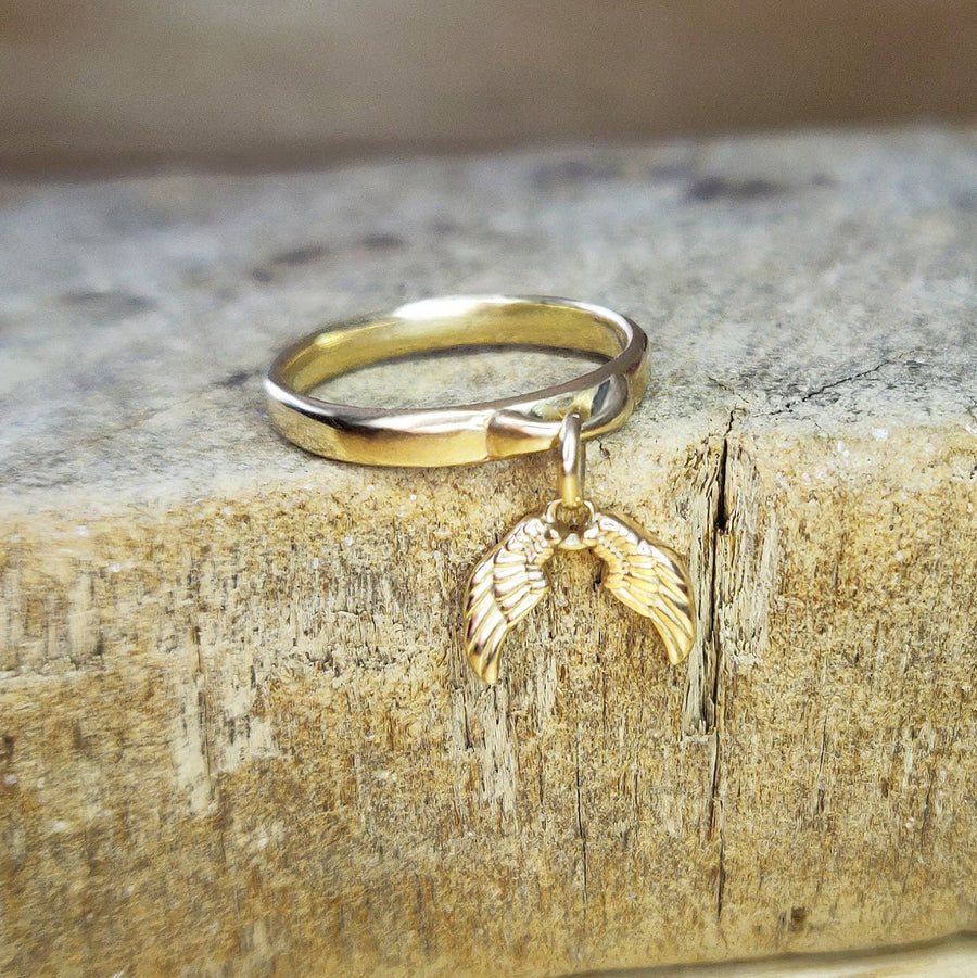 Gold Angel Wings Charm Ring on a wooden block