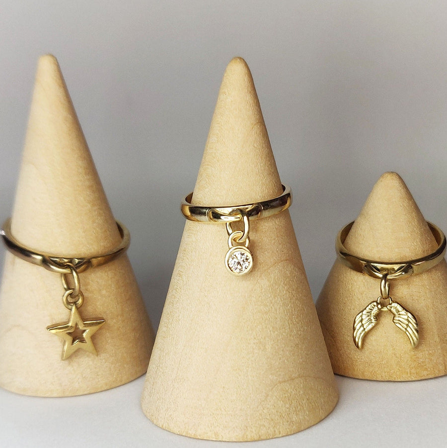 Yellow gold charms rings with angel wings, diamond and star gold charms on wooden display cones.