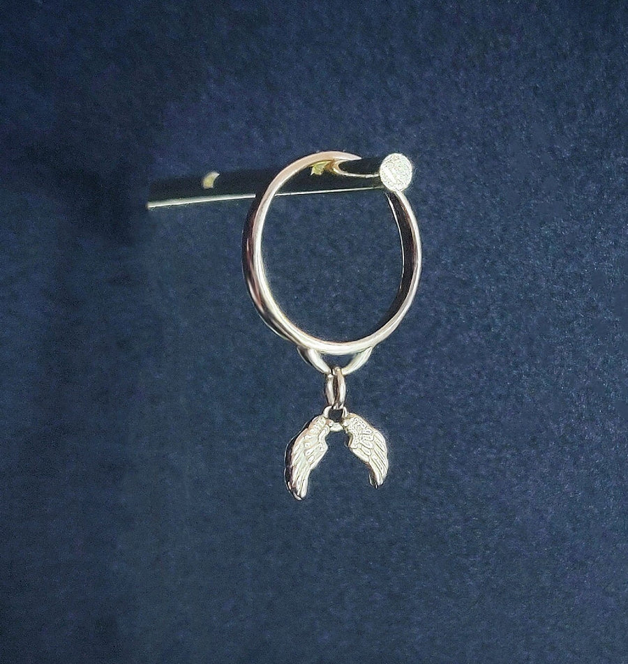 Solid gold dangle ring with angel wings charms, hanging against a blue background