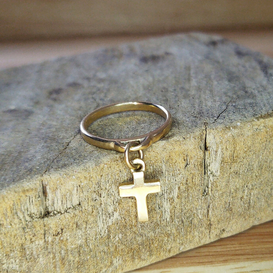 Solid gold dangly charm ring with a cross on a wooden block.