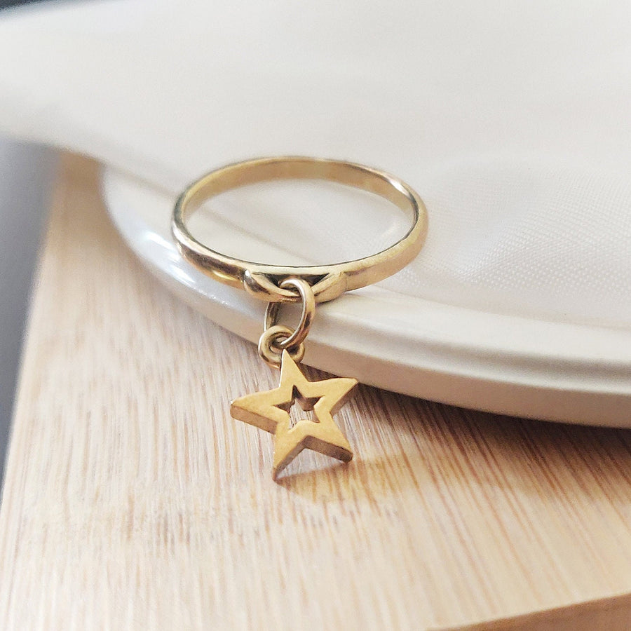 Solid gold dangle ring with a star charm on a dish