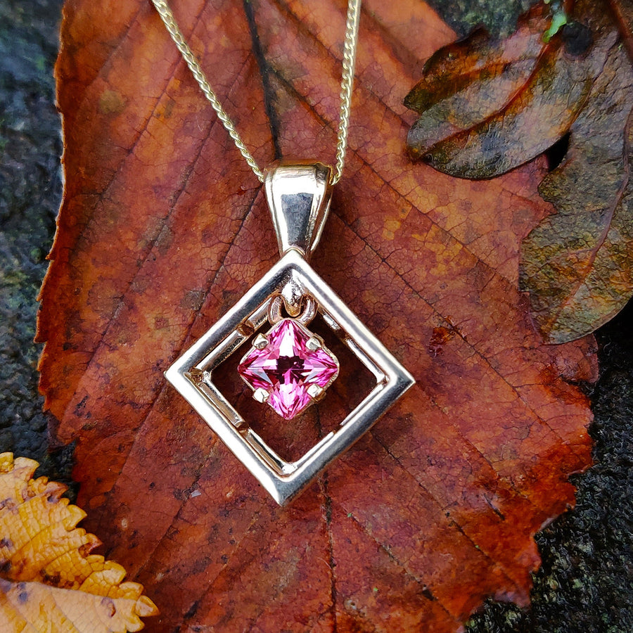 Solid gold pink sapphire princess cut pendant on a leaf.