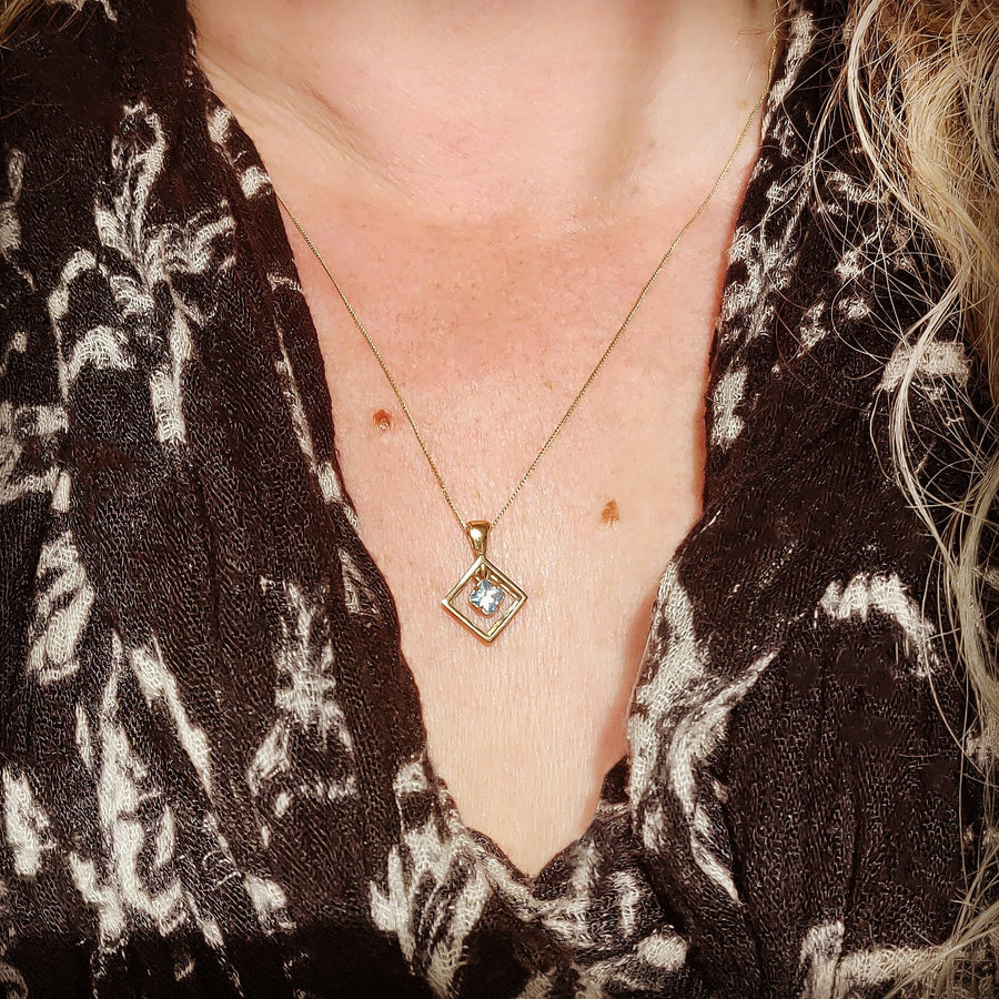 White sapphire diamond shaped gold necklace being worn.