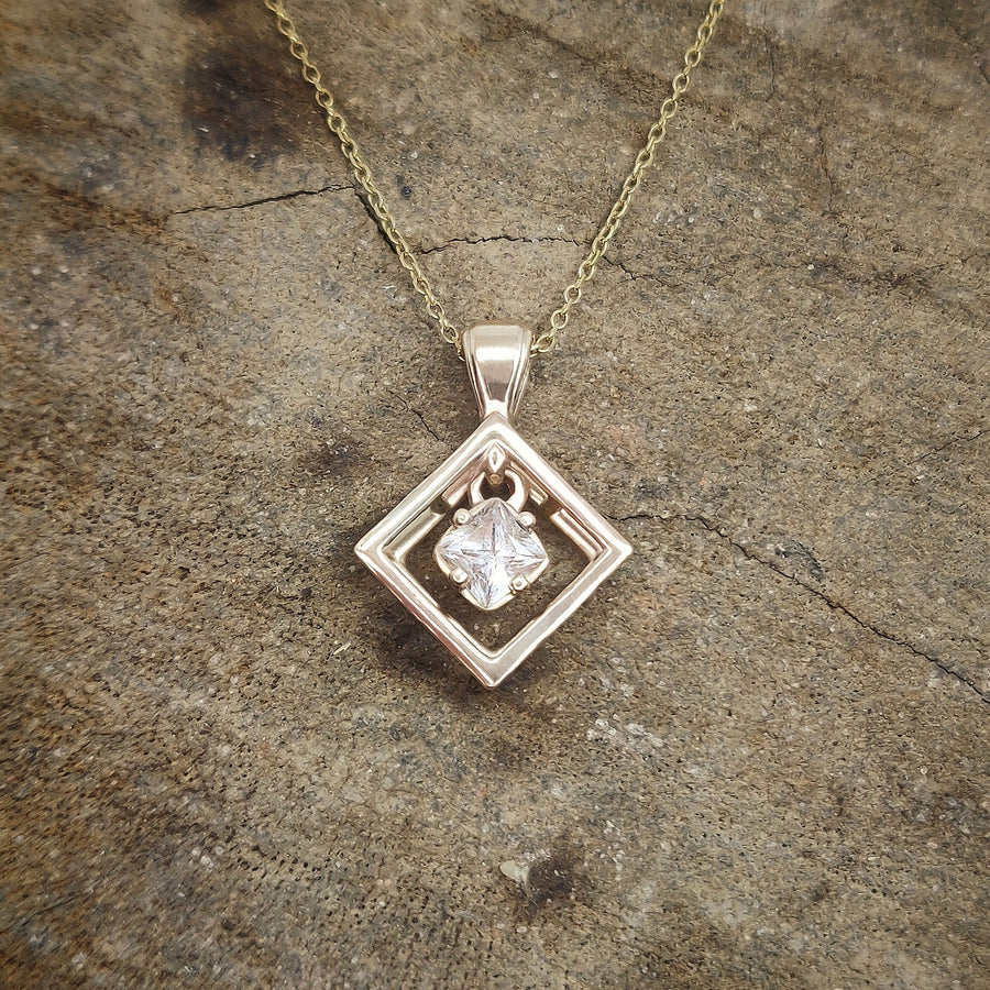 Yellow gold pendant and chain with a sapphire gemstone on a wooden block.