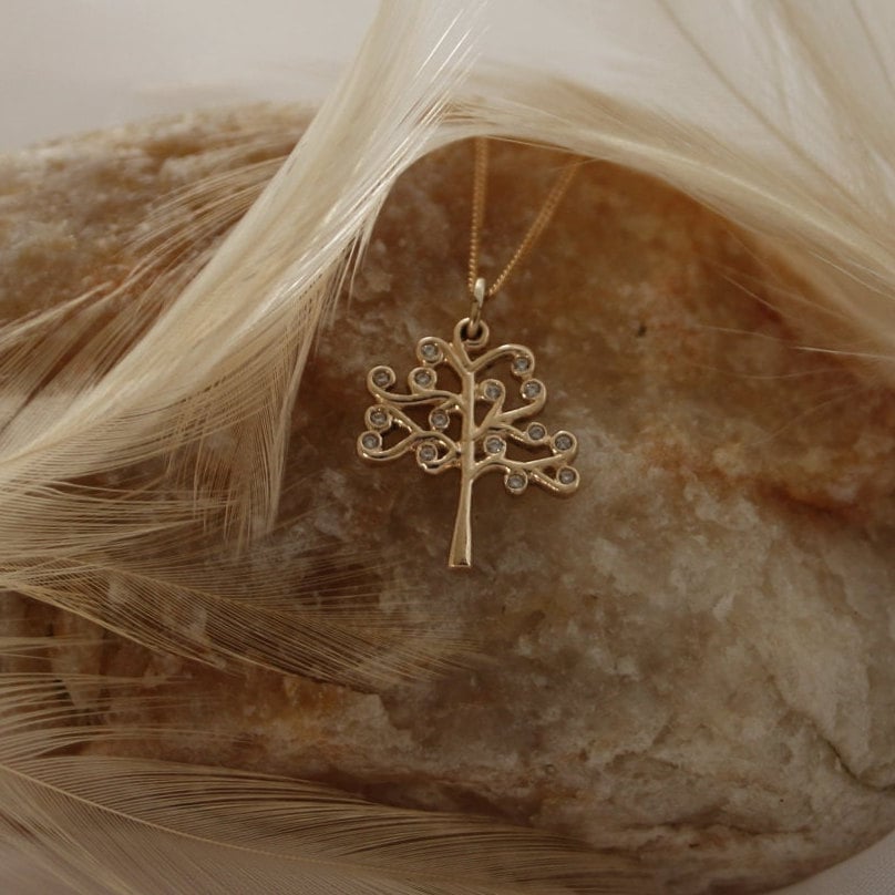 Gold tree of life pendant with diamonds on a rock display.