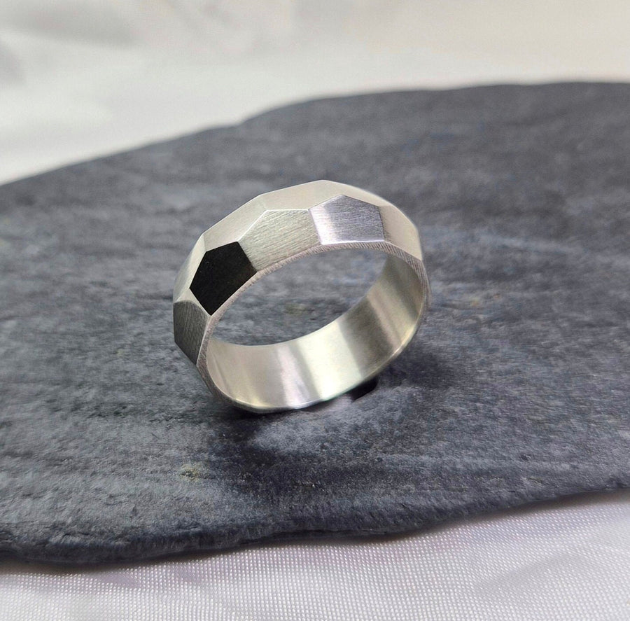 Silver chunky silver hammer texture wedding band standing on its side on a slate.