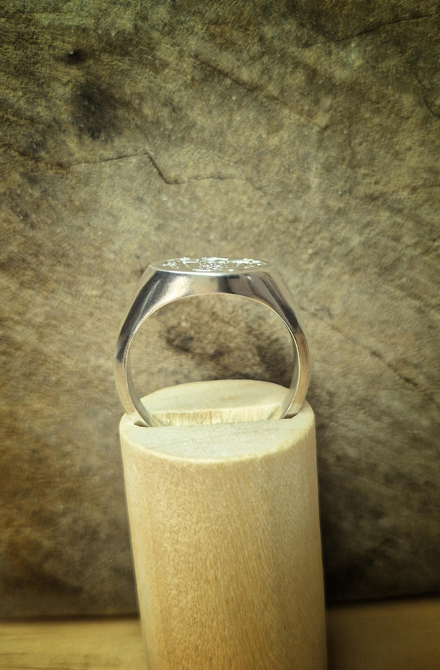 side view of an argentium sterling silver signet ring on a wooden stand.