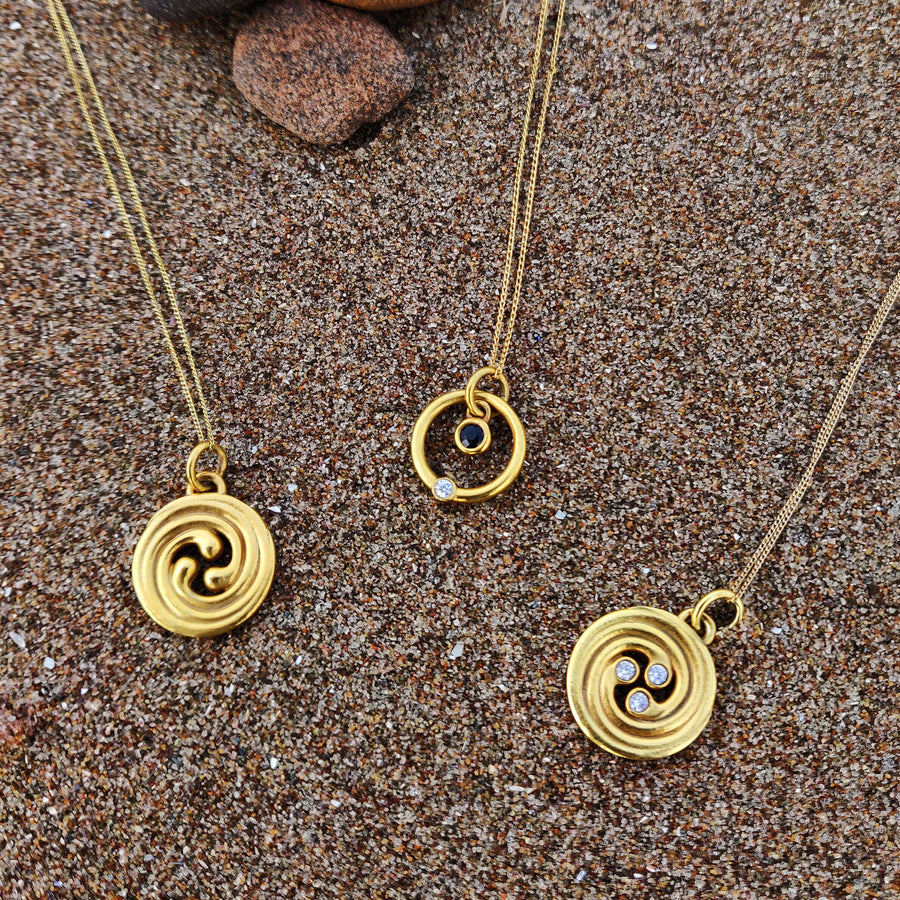 3 gold celtic necklaces laying in the sand.