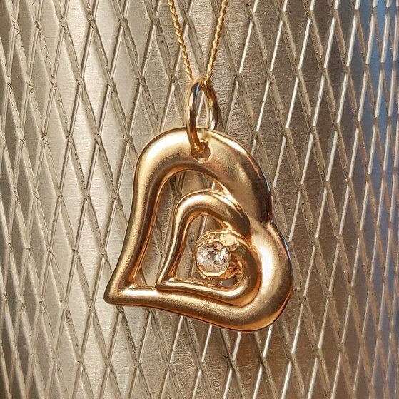 Gold and Diamond Heart Necklace in front of a silver background.