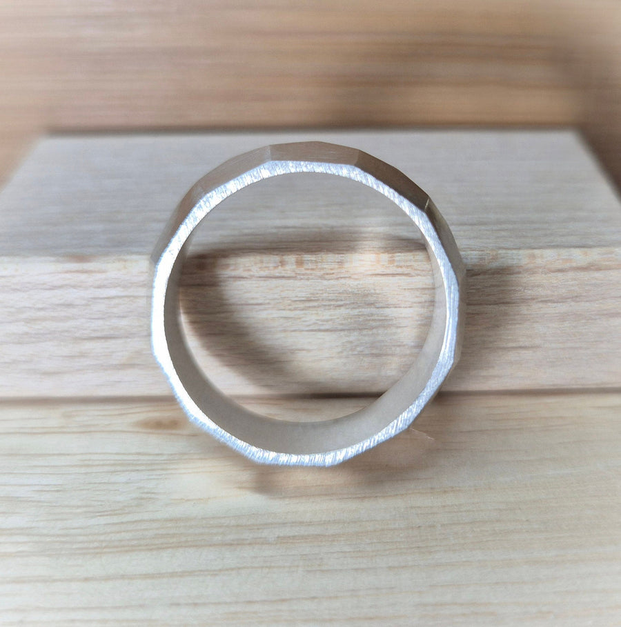 Side view of argentium sterling silver geometric wedding band against a wooden background.