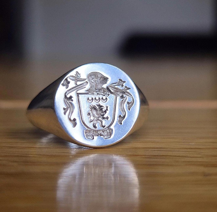 Reversed sigil coat of arms silver signet ring on a wooden background.