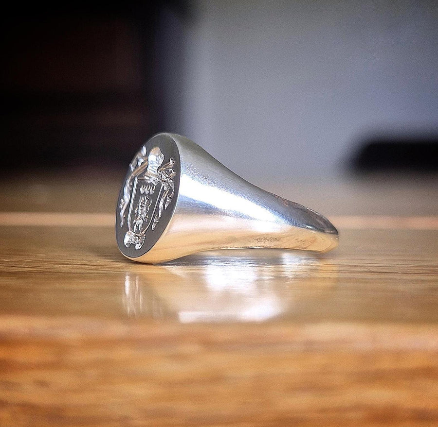 side view of a silver signet ring with family crest on a table