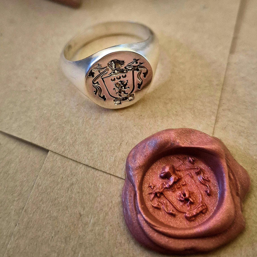 Silver signet ring with engraved sigil next to a wax family crest seal on an envelope.