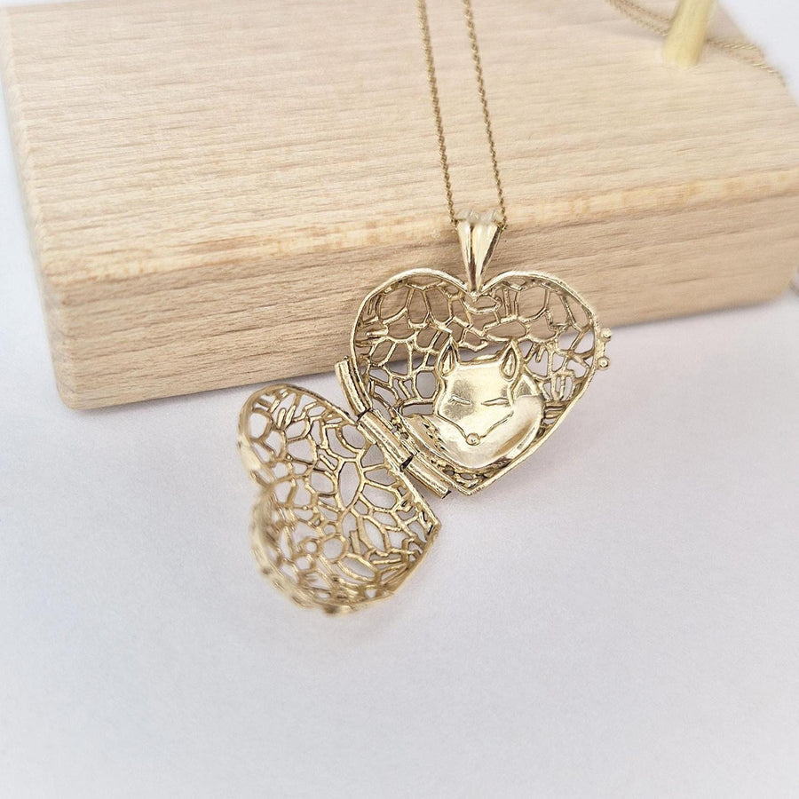 Open Sleepy Fox in a Hedgerow gold heart locket displayed on wooden stand, showing the sleepy fox curled inside its hedgerow pattern.