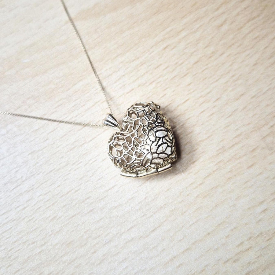 Closed gold filigree heart locket necklace resting on light wood, part of the Sleepy Fox in a Hedgerow jewelry line.