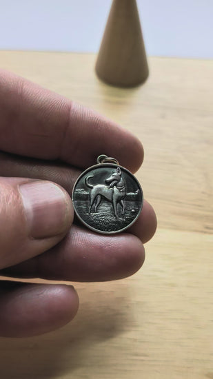silver dog pendant being shown to display size and thickness.